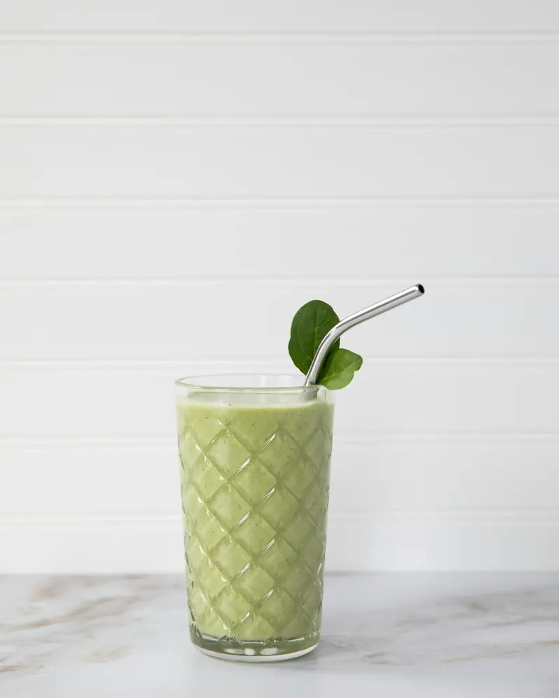 A green smoothie in a glass with a metal straw